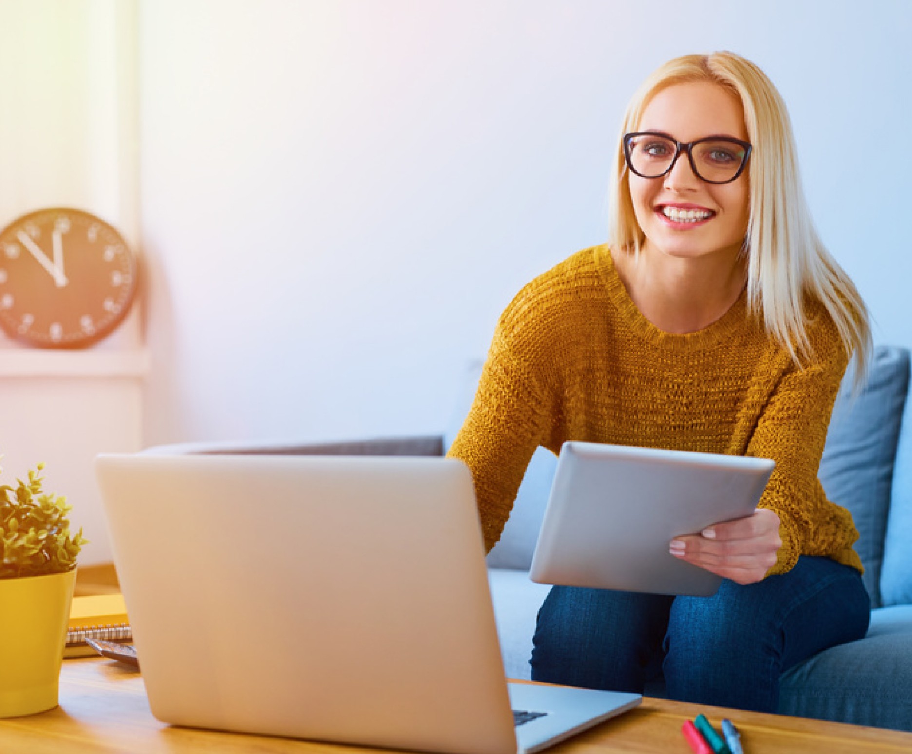 Eine Frau sitzt auf einem Sofa, hält ein Tablet und surft auf einem Laptop